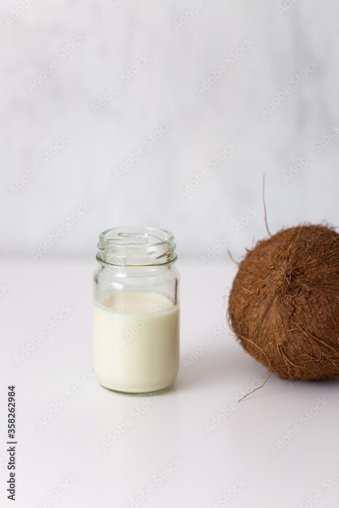 Coconut milk in a little jar and coconut on white marbl background with copy space Coconut milk in a little jar and coconut on white marbl background with copy space