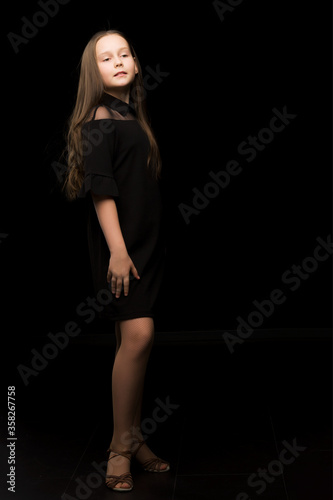 Cute little girl in a beautiful dress on a black background. © lotosfoto