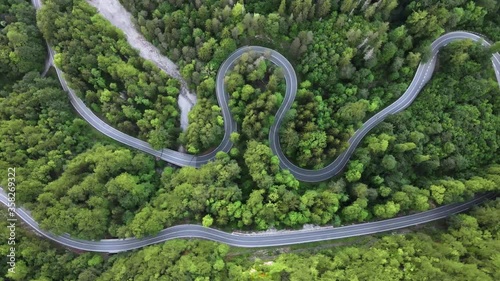 Aerial top down shot of biker riding on a curvy road in a lush green forest