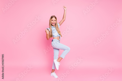 Full body delighted kid girl celebrate fortune lucky corona virus win raise fists scream eyah wear good look clothes isolated over pastel color background