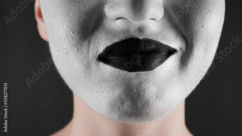 Portrait of a mime and bodypainting woman in white with black lips. Woman's lips on black background close-up photo