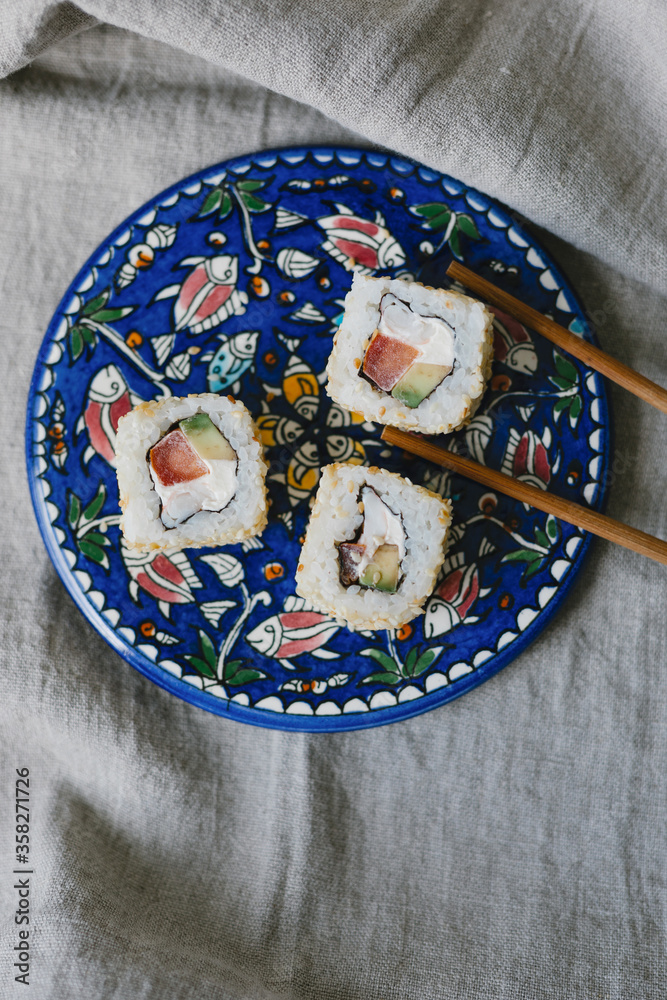 Sushi rolls on a blue plate with chopsticks on a gray background. Stylish composition with sushi.