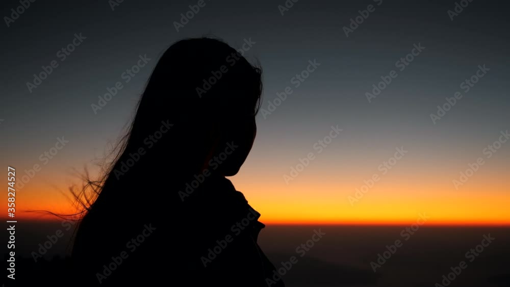 Hopeful Woman Looking at the Sunset on the top of a mountain at sunrise in slow motion. Silhouette of motivation feeling a dreamer girl looking hopeful at the horizon.