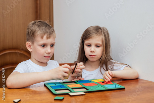 a boy and a girl of European appearance in light clothng sit and play a Board game photo