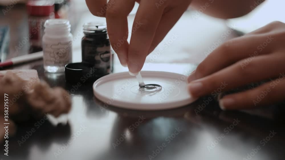 Close up shot of woman's hands mixing black and white colors in a plastic cap palette Close up shot of woman's hands mixing black and white colors in a plastic cap palette