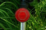 one red round plastic reflector on a gray metal bike pipe in green grass