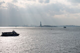 Freiheitsstatue mit Sonnenstrahlen und Touristenboot im Vordergrund