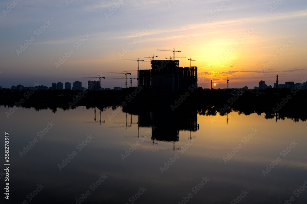 Beautiful urban construction site silhouettes at Dawn. Morning Cityscape with Reflection in lake water.