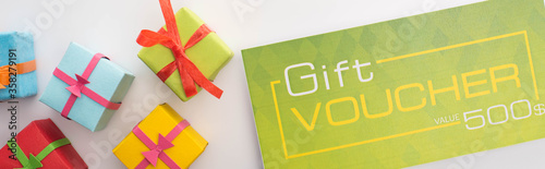Panoramic shot of gift voucher near presents on white background