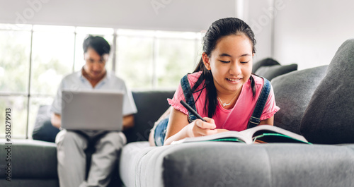 School kid little girl learning and making homework studying knowledge on book with father relaxing using laptop computer working and video conference meeting chat at home.work from home concept