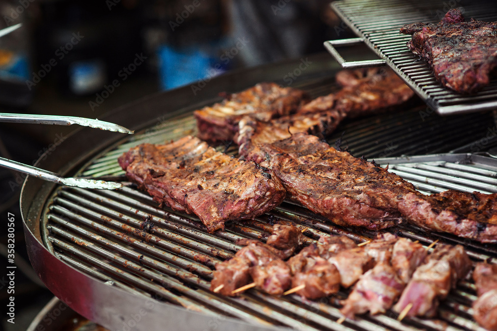 Fresh grilled meat. Street market. Chef preparing meat, close up. Chef with tongs holding hot pork ribs. Street food.