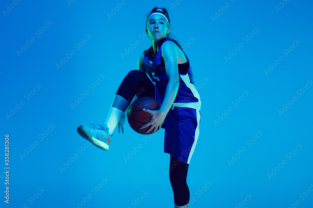 Unstoppable. Young caucasian female basketball player training, prcticing with ball isolated on blue background in neon light. Concept of sport, movement, energy and dynamic, healthy lifestyle.