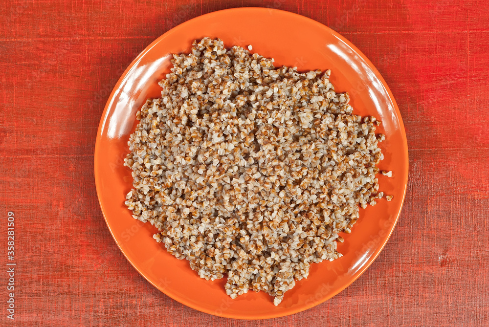 Buckwheat orange plate on a wooden table. Food in utensils on a background of old red plywood. Place for text near the plate. Copy space for design. Buckwheat orange plate on a wooden table. Food in utensils on a background of old red plywood. Place for text near the plate. Copy space for design.