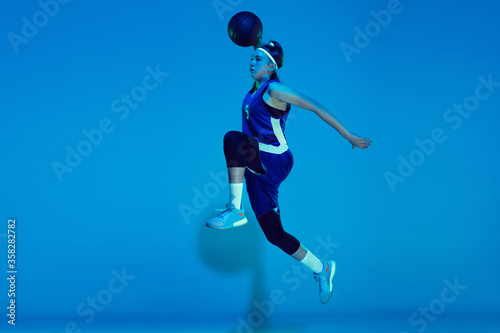 Leader. Young caucasian female basketball player training, prcticing with ball isolated on blue background in neon light. Concept of sport, movement, energy and dynamic, healthy lifestyle.