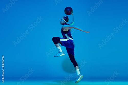 Leader. Young caucasian female basketball player training, prcticing with ball isolated on blue background in neon light. Concept of sport, movement, energy and dynamic, healthy lifestyle. © master1305
