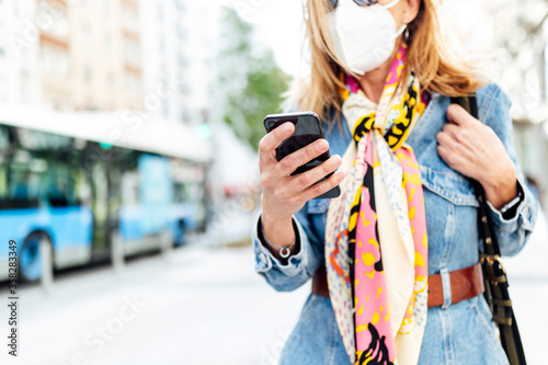 Woman using mobile phone in the street. She is wearing a protective mask for the prevention of a virus. Coronavirus concept