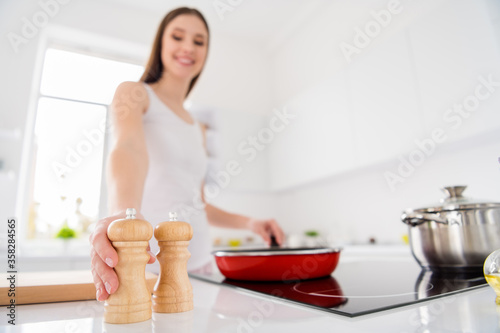 Blurred low angle view photo of positive chef brown hair girl frying veggie organic breakfast hold salt choose pepper for better flavor in kitchen house indoors