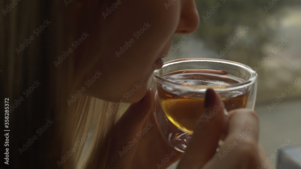 Beautiful young woman enjoying tea. Woman blowing on a hot tea Beautiful young woman enjoying tea. Woman blowing on a hot tea