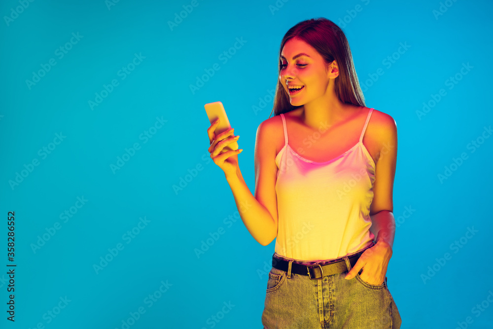 Chatting, texting. Caucasian young woman's portrait isolated on blue background in neon light. Beautiful female model in casual wear. Concept of human emotions, facial expression, sales, ad. Copyspace Chatting, texting. Caucasian young woman's portrait isolated on blue background in neon light. Beautiful female model in casual wear. Concept of human emotions, facial expression, sales, ad. Copyspace