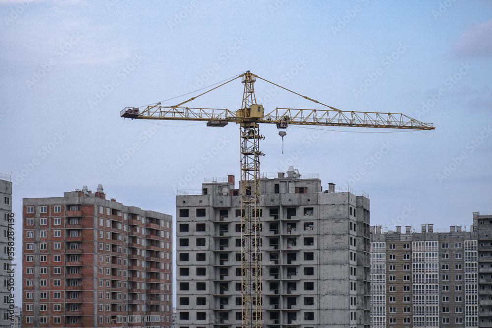 Multi-stage construction during the construction process with a yellow crane. Industrial background for design.