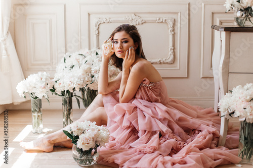 girl sitting on the floor in a lush pink dress and surrounded by fresh peonies