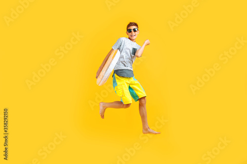happy excited teenager in sunglasses and a summer hat, having fun and jumping, holding an inflatable ring on a yellow background