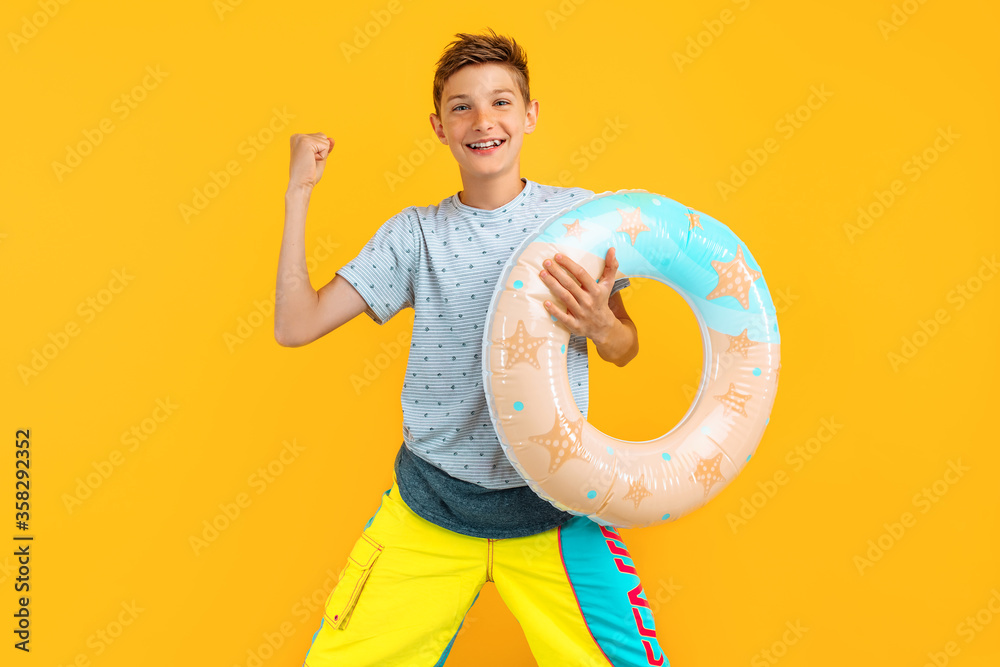 Happy teen guy, standing with an inflatable sea circle and celebrating victory, isolated on a yellow background Happy teen guy, standing with an inflatable sea circle and celebrating victory, isolated on a yellow background