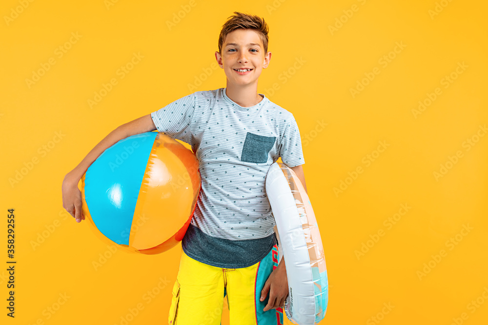 Happy teen guy, standing with a beach ball and an inflatable sea circle, isolated on a yellow background