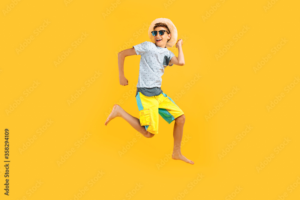 happy excited teenager in sunglasses and a summer hat, having fun and jumping, on a yellow background