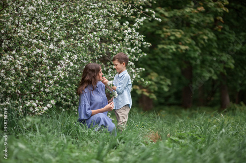 Happy and beautiful mother and son in clothes of blue tones are hugging next to a blossoming apple tree. The concept of spring, motherhood, happy family, relationships.