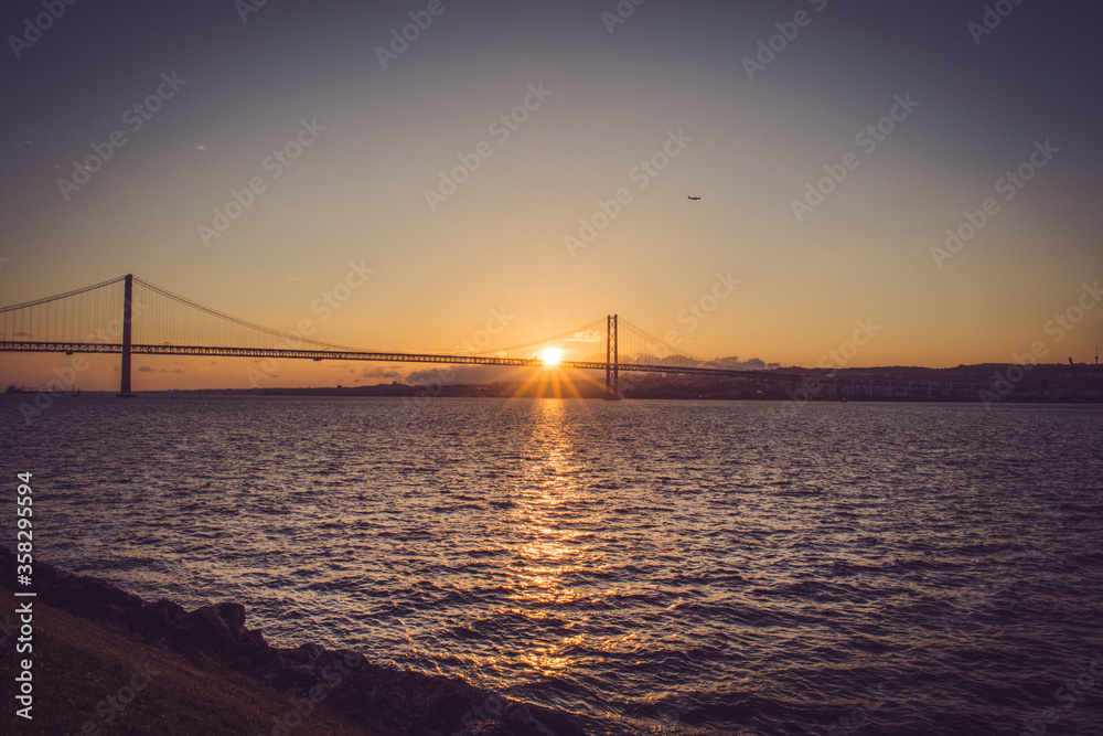 sunset rays over a large bridge that stretches over a wide river