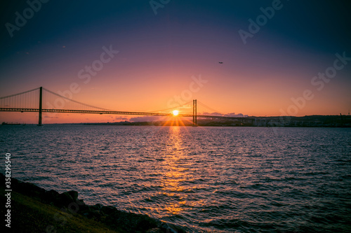 sunset rays over a large bridge that stretches over a wide river