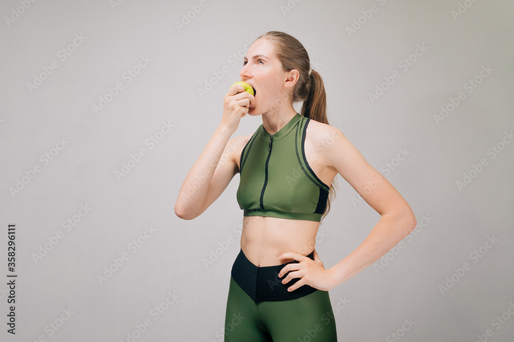 Athletic girl bites green apple. Fitness bikini athlete eats before training. Model is starving Athletic girl bites green apple. Fitness bikini athlete eats before training. Model is starving