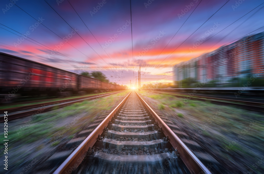 Railroad and beautiful sky with clouds at sunset with motion blur effect in summer. Industrial landscape with freight train, railway station and blurred background.  Railway platform in speed motion