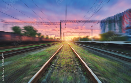 Railroad and beautiful sky with clouds at sunset with motion blur effect in summer. Industrial landscape with freight train, railway station and blurred background. Railway platform in speed motion