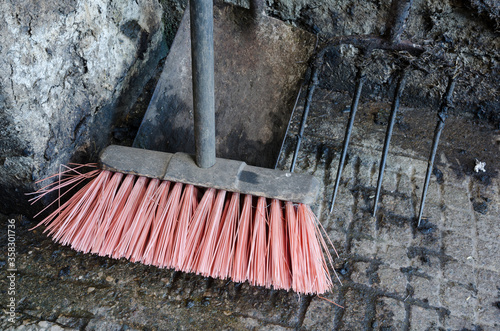A vibrant pink bristled sweeping brush in a concrete cattle shed. Cold and dirty cattle shed cleaning and sweeping broom head. pink brush bristle tip.