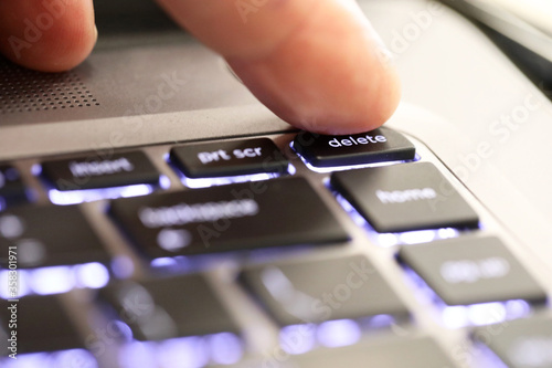 Foto close up of a finger hitting pushing the delete symbol button tab on an illuminated laptop computer key board