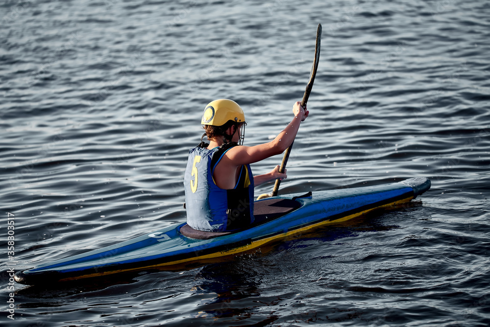 A guy wearing a helmet on a canoe polo rowing a paddle and sailing on water. canupolo. puts on a rescue yellow. rear view