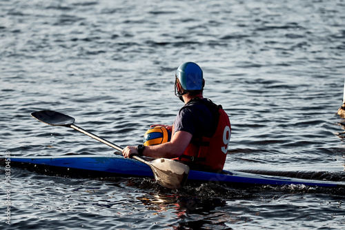A guy wearing a canoe polo helmet rowing on a paddle and sailing on water with a ball in his hands. canupolo. puts on rescue yellow. rear view