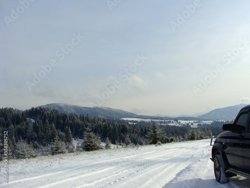 Modern SUV on a winter road. Family trip to the mountains by jeeps. Winter holidays at a ski resort in the Carpathians concept. Coniferous trees on a snowy mountain peak covered with hoarfrost