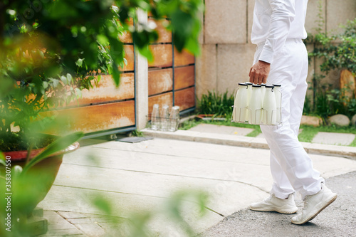Unrecognizable milkman in white uniform delivering milk to his customers and taking back empty glass bottles in morning, copy space