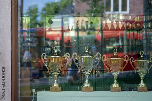 A street view at Trophy cups lined on a shelf throw the window of a shop.