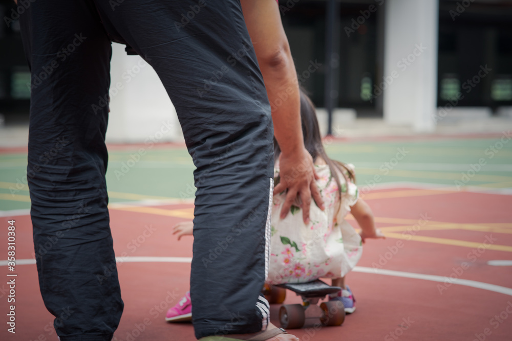 Obraz premium Adult pushing toddler on skateboard in the park. view from behind. Learning and family concept.