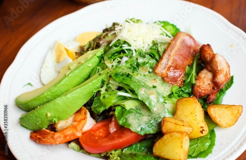 Colorful salad with tomatoes, avocado, lettuce, eggs, ham, chicken, potatoes and cheese on a white plate