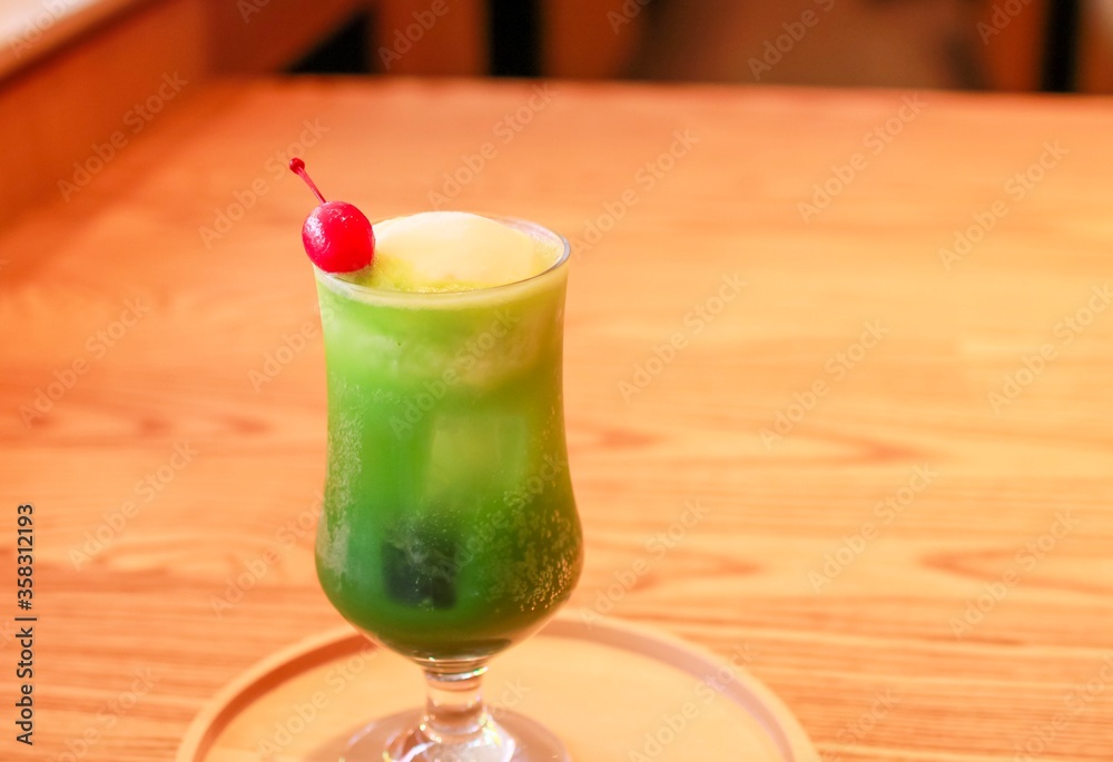 Matcha float drink (cold matcha drink with vanilla ice on top) on a wooden plate on a wooden table with a cherry Matcha float drink (cold matcha drink with vanilla ice on top) on a wooden plate on a wooden table with a cherry