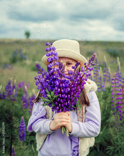 Beautiful girl 5 years old in a straw hat in a field of lupins