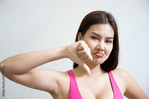unhappy upset woman giving thumb down; negative angry upset failed asian woman showing rejecting thumb down; negative denying thumb down gesture; asian woman young adult model