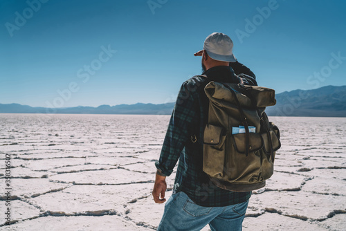 Young male traveler with backpack looking at trekking route explore death valley on vacation, back view of hipster guy wanderlust fascinated with breathtaking scenery of desolate desert lands. © BullRun