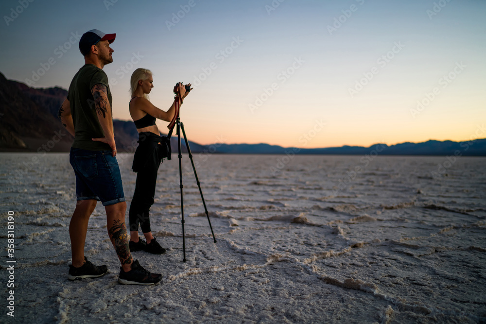 Skilled male and female photographer  colleagues shooting video in desert of Badwater using modern equipment for night pictures, hipsters friends wanderlust making photos of nature landscape
