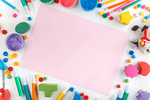 Top view of white tabletop with various drawing tools, finger paints, toy cow, white paper sheet. Mock up. Children's drawing table.